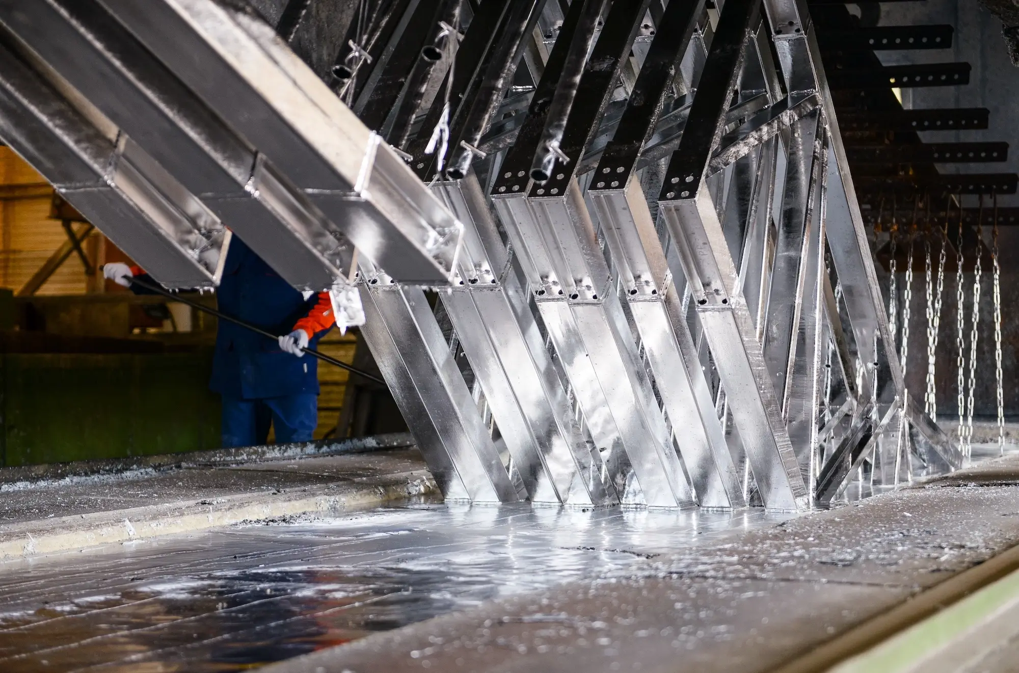 Dipping massive steel beams into molten zinc to ensure long-term rust protection.
