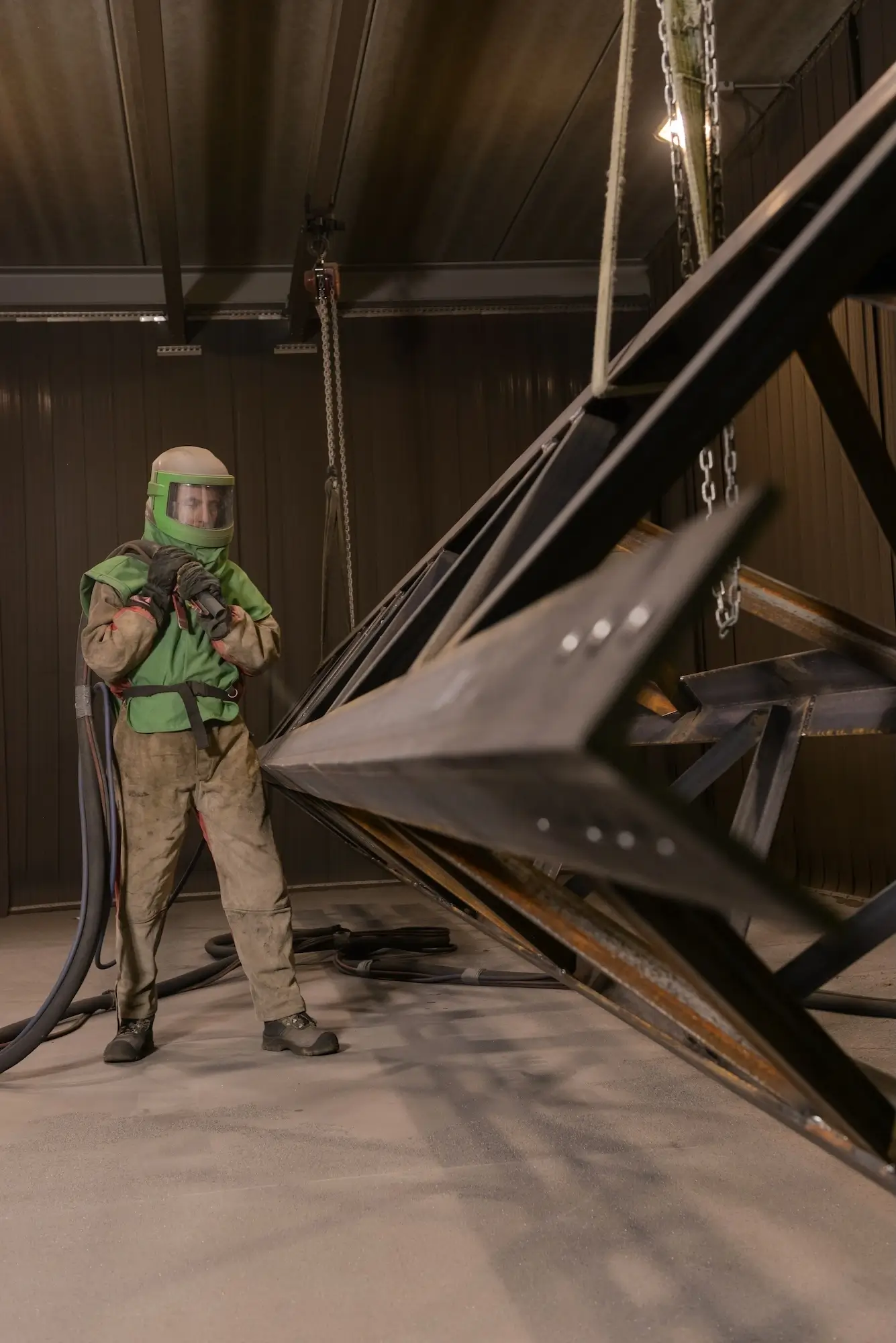 Manual cleaning and processing of an industrial metal structure in a shot blasting chamber.