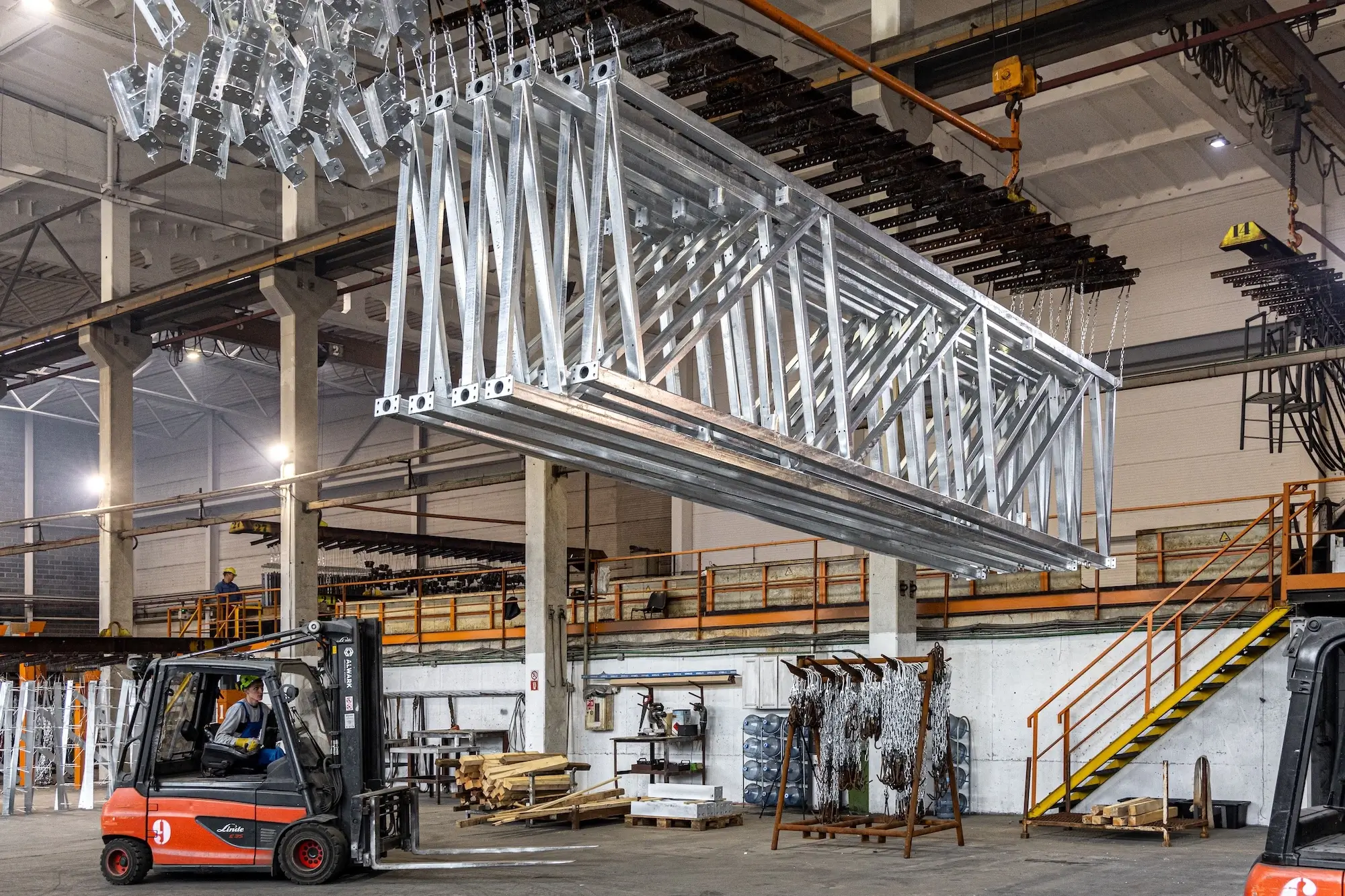 Moving a large-scale galvanized metal truss in the factory warehouse using a forklift.